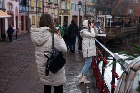 Colmar - France - 2 January 2022 - Portrait on back view of tourist taking a photo with her smartphoneのeditorial素材