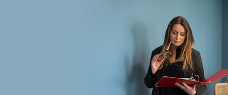 Portrait of young woman with eyeglasses and red file in hands on blue wall background