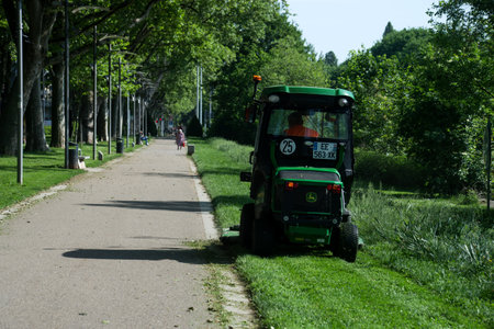 Mulhouse - France - 12 May 2022 - municipal employee driving green tractor and lawn mower, shears lawns in urban parkのeditorial素材