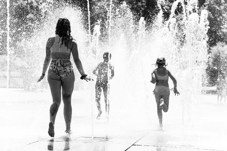 Colmar - France - 12 July 2022 - Portrait of girl wearing swimsuit running and splashing in a public fountain in the street in black and whiteのeditorial素材