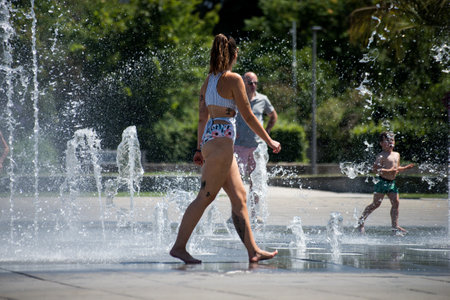Colmar - France - 12 July 2022 - Portrait of girl wearing swimsuit walking and splashing in a public fountain in the streetのeditorial素材