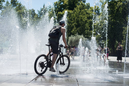 Colmar - France - 12 July 2022 - Portrait of man with bicycle splashing in a public fountain in the streetのeditorial素材