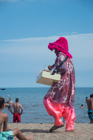 Valras - France - 28 July 2022 - Portrait of colorful beach seller walking on the sandのeditorial素材