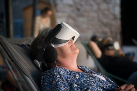 Portrait of woman watching in an interactive glasses of virtual reality sitting in outdoorの写真素材