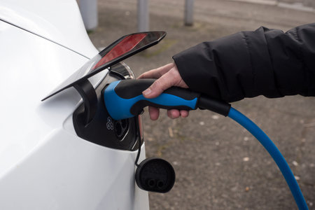 closeup of hand of woman charging a white electric car parked in the streetの写真素材