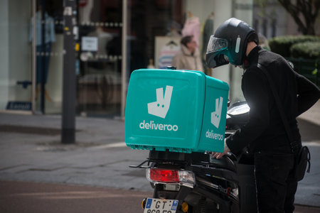 Mulhouse - France - 10 April 2024 - portrait of delivery man standing in the street near his deliveroo scooterのeditorial素材