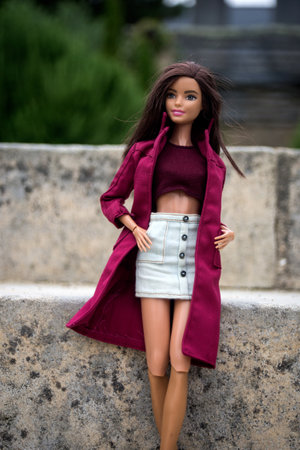 Quimper - France - 13 July 2024 - Portrait of brunette barbie doll wearing a red coat standing in a public gardenのeditorial素材