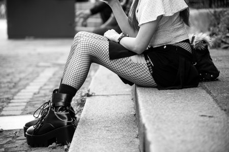 Closeup of legs of gothic girl wearing sexy stockings and black boots sitting in the streetの写真素材