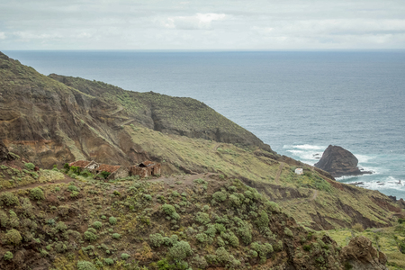 Steep high lava rock cliffs on on the east of Tenerife. Solitary rocks sticking out of the water. Old abandoned huts. Blue sea horizon, natural sky background.の写真素材