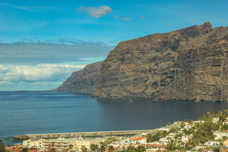 View of the Los Gigantes port and volcanic cliffs on the west coast of the Tenerife island. Sunny day, clear blue sky with little clouds.の写真素材