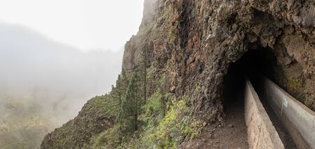 An old aqueduct now used as an adventure hiking trail Guimar valley. Trail in the fog through the mysterious mountains and caves. Tenerife, Spain.の写真素材