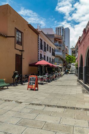Puerto de la Cruz, Tenerife, Spain - July 10, 2019: Colourful houses and palm trees on streets. People relax and have fun on a warm sunny summer day. Have breakfast, drink coffee in a cozy cafe.のeditorial素材