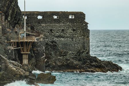 Vallehermoso beach in La Gomera with Huge waves crashing on basalt rocks. Old stone building named El Castillo del Mar, an old banana factory. Shot by long focus lens. Canary Islands, Spain.の写真素材