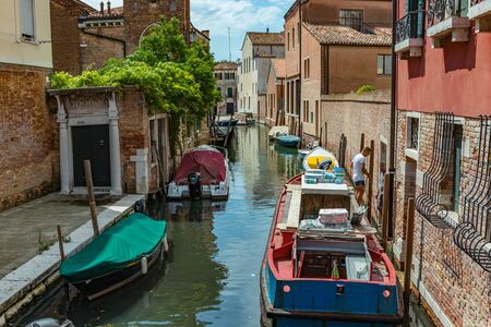 VENICE, ITALY - August 02, 2019: One of the thousands of lovely cozy corners in Venice on a clear sunny day. Locals and tourists strolling along the historical buildings and canals with moored boats.のeditorial素材