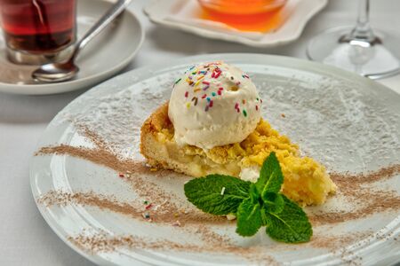 Piece of cake charlotte with apples ice cream ball and fresh mint on white plate. Served with a...