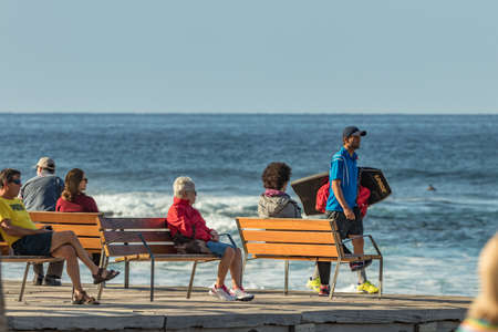Las Americas,Tenerife, Spain - January 21, 2020: People on the waterfront, walking on promenade and relax sitting on benches near the sea on blue sky background. Popular tourist resort, Canary Islandsのeditorial素材