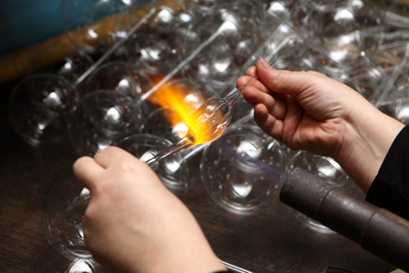 Factory of Christmas toys. The worker blows out the glass. The burner melts the glass. Decoration of a Christmas tree toy. Handmade. Manufacture of fur-tree toys. Many beautiful glass beads. Burning products in the oven.の写真素材