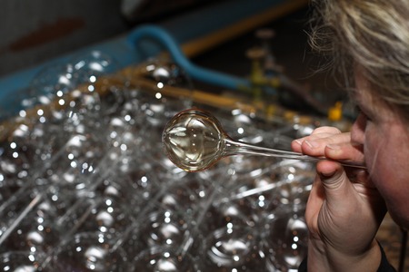 Factory of Christmas toys. The worker blows out the glass. The burner melts the glass. Decoration of a Christmas tree toy. Handmade. Manufacture of fur-tree toys. Many beautiful glass beads. Burning products in the oven.の写真素材