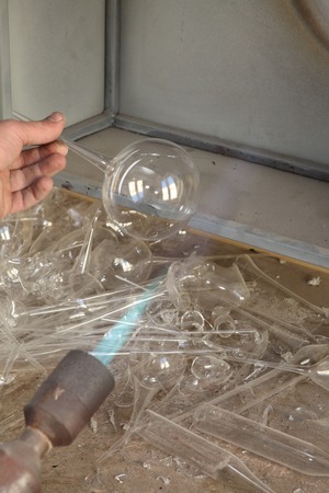 Factory of Christmas toys. The worker blows out the glass. The burner melts the glass. Decoration of a Christmas tree toy. Handmade. Manufacture of fur-tree toys. Many beautiful glass beads. Burning products in the oven.の写真素材