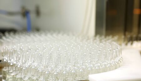 Visual control of ampoules with medicine. A woman works on an ampoule production line. Sterile bottles and ampoules on the dispensing line. Sealed ampoules with medicine. Sterile capsules for injection. Bottles on the bottling line of the pharmaceutical.の写真素材