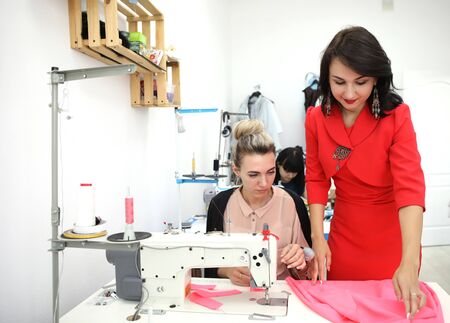 Beautiful girl in a red dress in a tailoring studio. Exclusive tailoring of dresses to order. The...