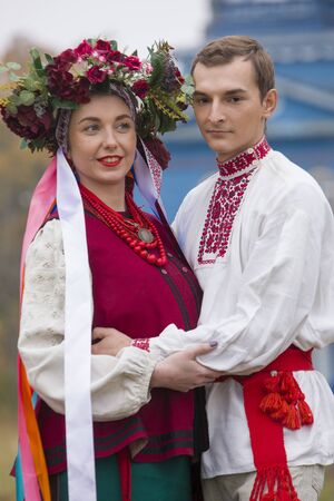 Girl and guy in retro costumes on the street in the old village. Retro staging of an ancient rite. Beautiful wreath on a girl. The guy hugs the girl, both are smiling. Antique clothing of the late 19th centuryの写真素材
