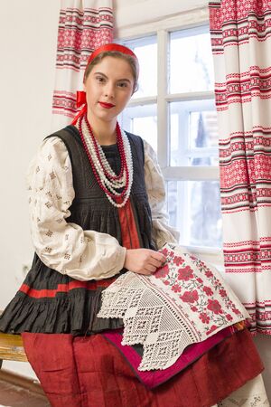 Beautiful young girl in a national costume of the 19th century. Embroiders a beautiful pattern near...