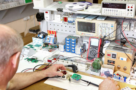 Service center for the repair of power voltage relays. Human checking electrical device with digital display. Numbers on the test bench. Manufacture of sockets volt control and quality control..の写真素材