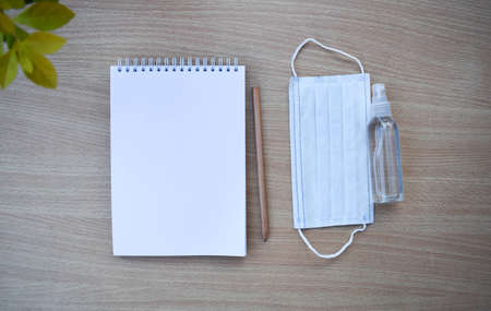 A blank notebook with face mask and alcoholic hand sanitizer on the workspace of the work table. Top view with copy space.の写真素材