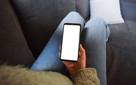 Image of a woman holding a mobile phone with a blank screen while sitting on the sofa with a feeling...