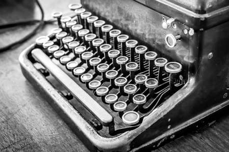 Old vintage typewriter on a wooden table. Black and white photo.