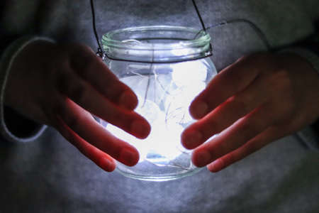 A person's hand holds a glass jar with light inside, close-upの写真素材