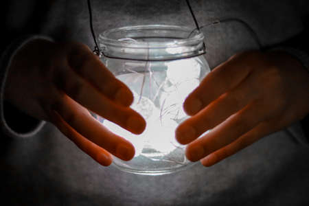 Hands holding a glass jar with a light inside. Conceptual image.の写真素材