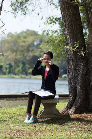 Thai woman calling using phone under big treeの写真素材