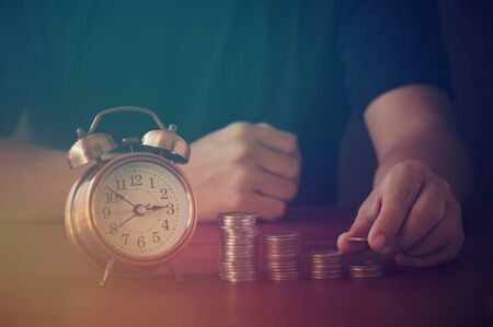 hand  put money on pile of coin on table in dark tone;の写真素材