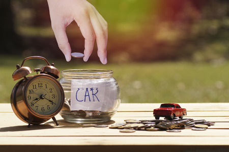 hand put money in glass bottle to save for  buying car with clock on wood tableの写真素材