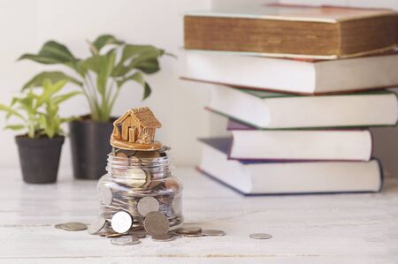 house with coins , plant and book background on table, concept in buying, loan and selling home