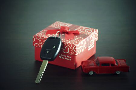 car key on a paper box with red ribbon bow on black natural wooden table background. Birthday's Day gift or present abstract concept.の写真素材