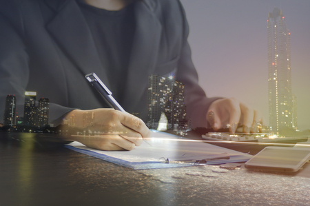 double exposure of Businesswoman Hand Calculating Invoice Using Calculator At Desk In Office  and  nigt city, concept in finance, account and capital bankingの写真素材