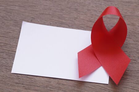 red ribbon and white empty paper on the wooden background, AIDS sign with copy spaceの写真素材