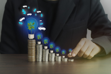 businesswomen put money on pile of coins with green tree and light bulb, concept in finance, loan and buying in business about carの写真素材