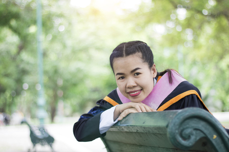 Happy and glad graduated Asian student siting on arm shair in park, congratulations, graduate education success, concept education and finished learning in classの写真素材