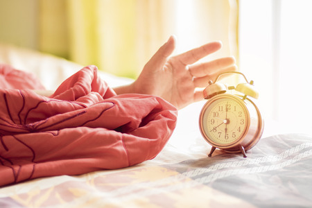 hand stop alarm clock on bed at 6 o'clock