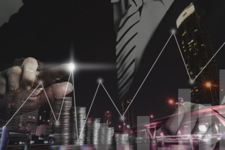 double exposure hand of businessman  point at light of graph on money coins and night city for...