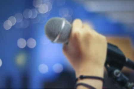 Defocused and blur of hand holding microphone on bokeh background, concept as music instrument in studio room and meeting hallの写真素材