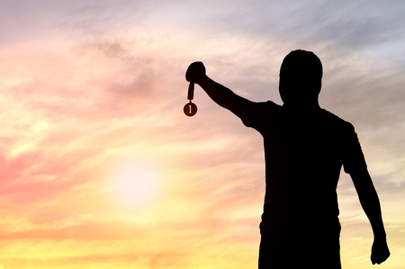 Silhouette of man holding Golden Medal on sunset background, concept as winner and champion in sport and businessの写真素材