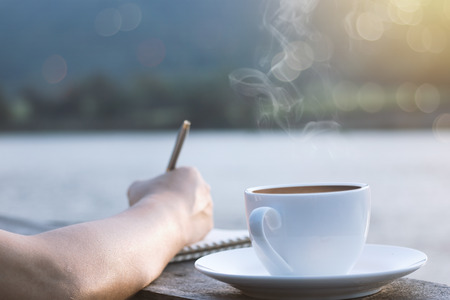People writing and planning work on wooden balcony and cup of hot coffee for brackfast near river and mountain backgroundの写真素材