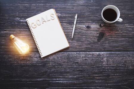 idea and innovation concept, light bulb with note book for goal and target writing and planing in new year on table in dark toneの写真素材