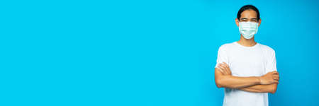 Asian delivery man wearing mask holding parcel box and show screen of phone on blue background in...