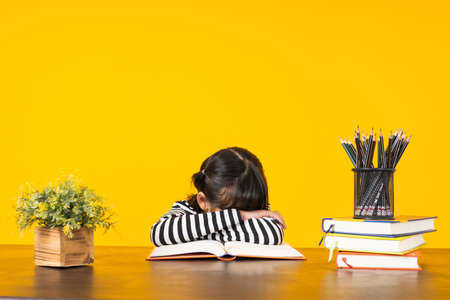 Kid sleep on table with lots of books on yellow background in studio